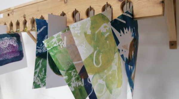 A selection of gelli prints hanging in a marble drying rack
