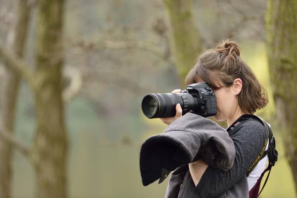 Image shows a woman in the woods with a camera taking a photo