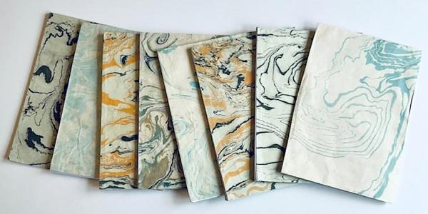 A selection of marbled paper in shades of blue, orange and cream laid out on a white background.