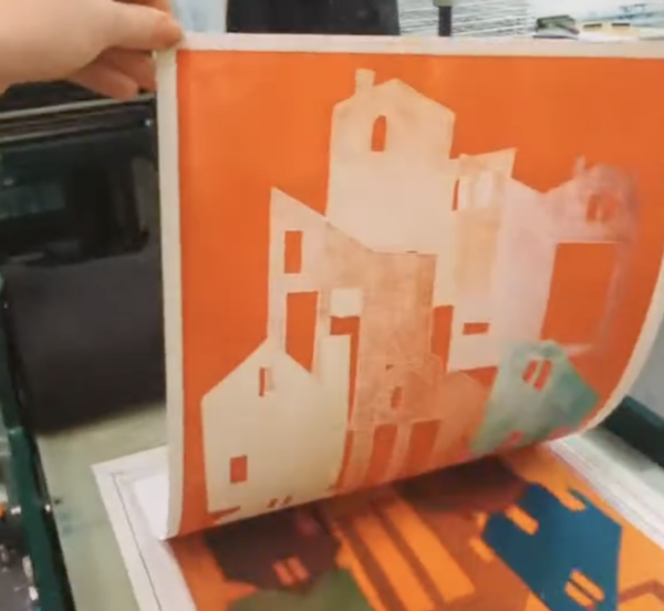 A monoprint of buildings in orange being revealed.