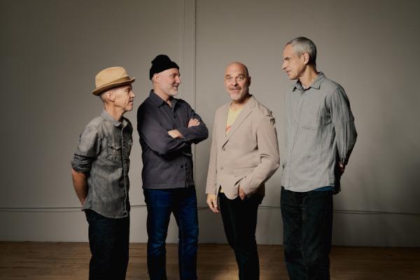 Four men; the members of The Bad Plus, standing together in an indoor setting.