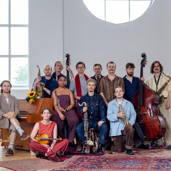 The Ancient Infinity Orchestra lined up and holding their respective instruments in a bright room laden with rugs.