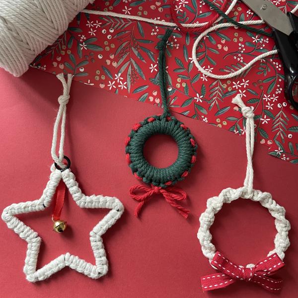 A photograph of a flatlay of 3 macrame decorations on a red background. 2 beige ones and 1 green ones.