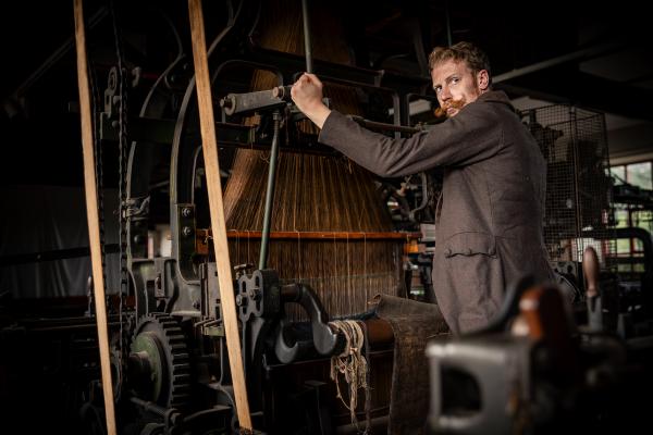 a man with a large moustache in a brown jacket using a large industrial machine in Leeds Industrial Museum
