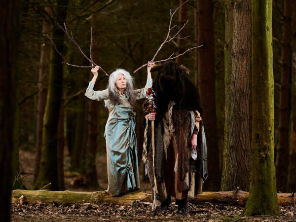 Two people in elaborate costume stand in a forest