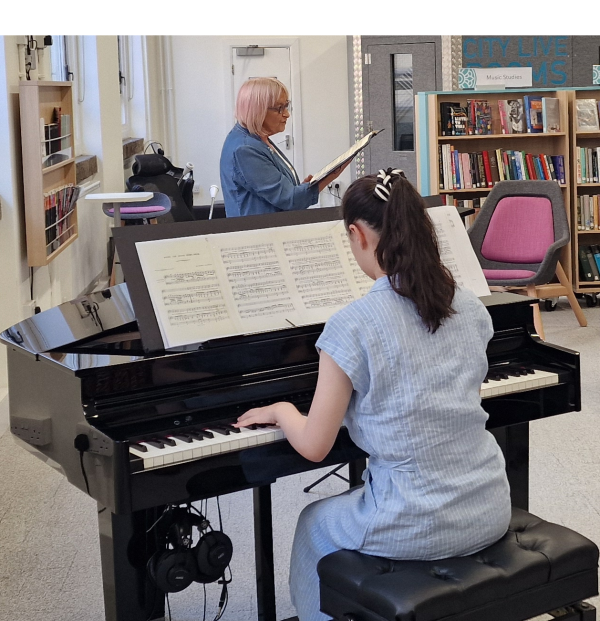 woman in blue dress plays piano whilst another woman with light pink hair sings .