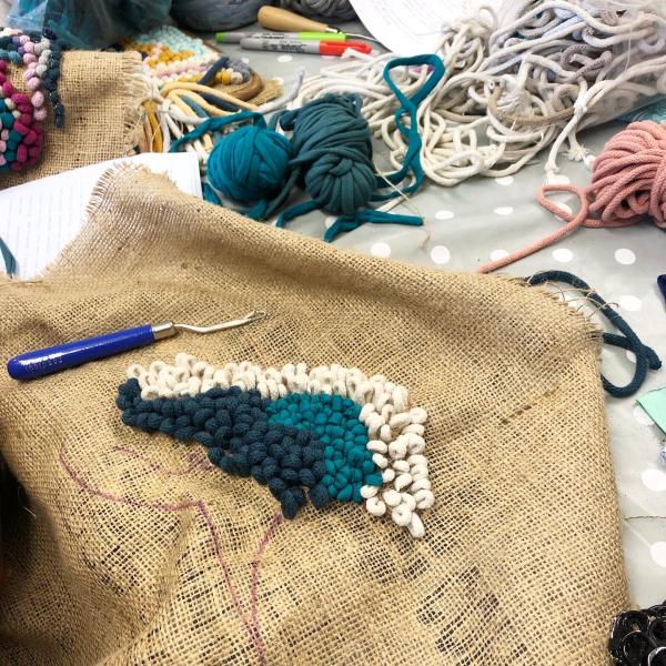 Image shows little loops made from cotton cord on hessian with a blue latch hook and cord scraps in the background.