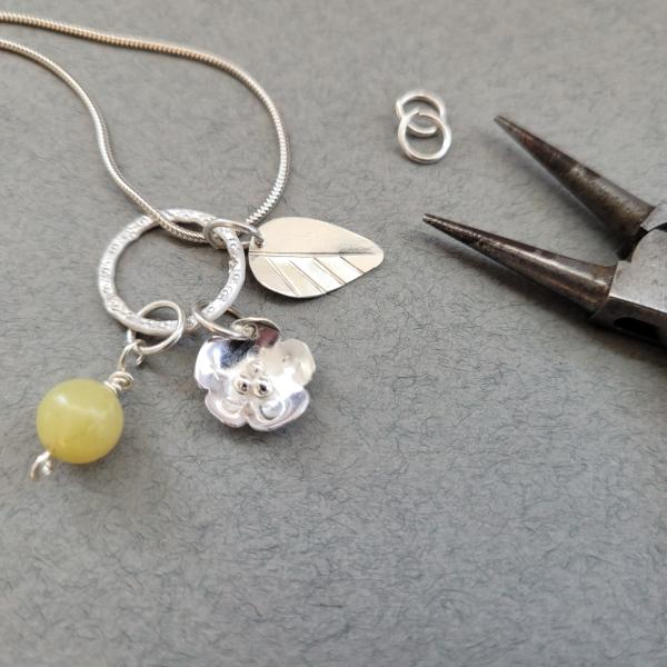 A photograph of a charm necklace laid against a grey backdrop with a pair of pliers