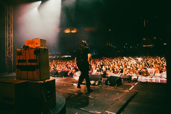 An artist playing music on a big stage during a concert with a crowd in the background