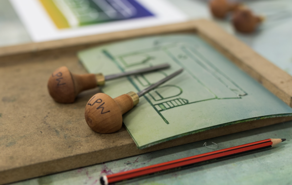 Lino cutting tools and a pencil with a piece of lino depicting a building
