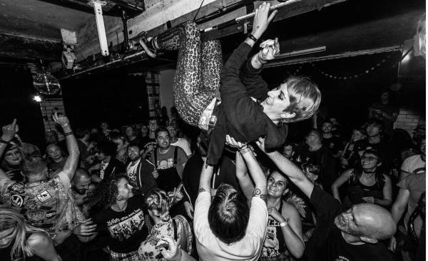 Punk woman hanging from a girder over happy crowd at rock gig