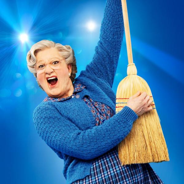 Mrs Doubtfire wearing her classic blue cardigan and skirt holding holding up a broom as if it's a guitar.