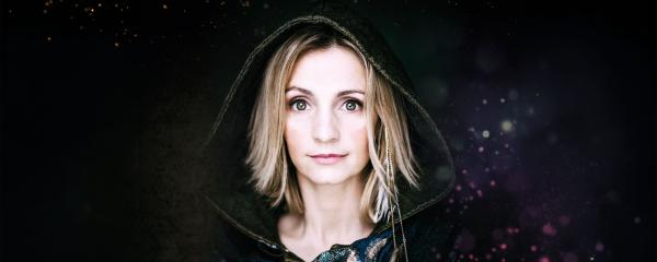 A women with medium length light coloured hair, wearing a black hooded robe.