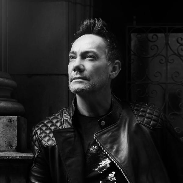 Black and white image of Craig Revel Horwood looking pensive wearing a black leather jacket.