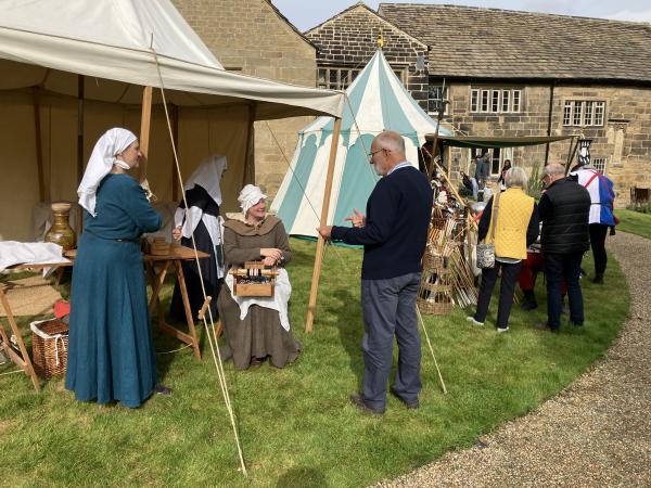 Historical Re-enactors dressed as Tudor era people sit in medieval style tents speaking to visitors. The tents are on a lawn in front of Tudor medieval manor house, Calverley Old Hall.