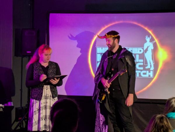 two people on a stage, one holding a book, another holding a guitar