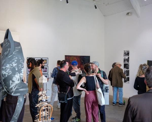 A group of people can be seen in a gallery space, surrounded by wall hangings