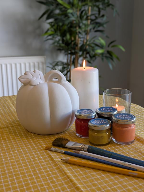 image of a ceramic pumpkin with paint brushes and pots of paint next to it ready to paint