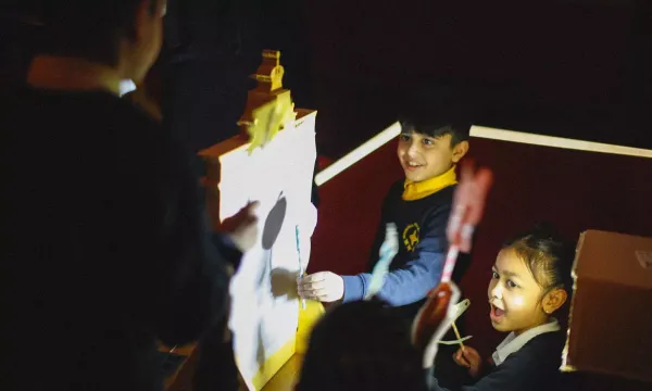 Several young children performing a shadow puppet play, with homemade puppet shapes.