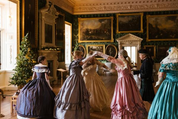 Image of multiple women dancing in historic ball gowns within a ball room