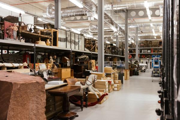 Image of a large warehouse containing museum collection objects, such as a rocking horse, taxidermy and furniture.