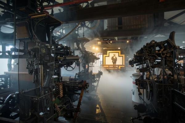 Photograph of a factory with industrial machinery, with ambient smoke obscuring the background.