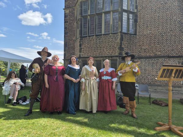 The are 4 female dancers and 2 male musicians in civil war outfits are stood in the garden at Temple Newsam house.