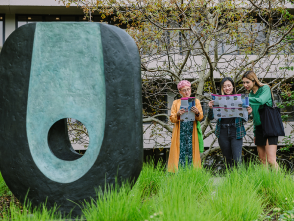 Three people looking at maps stood outside next to an oval shaped blue and black sculpture.