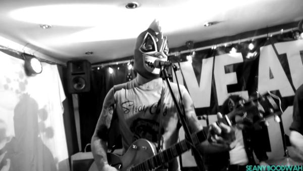 A black and white image of a man playing guitar with a spooky mask on.