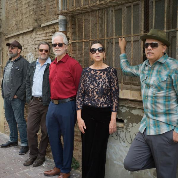 Members of The Delines all wearing sunglasses and casually posing along a brick wall.
