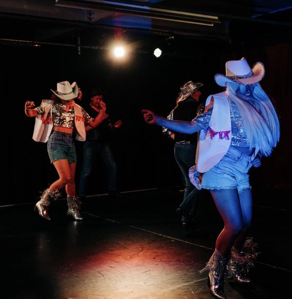 Low light photo of 2 women leading the Decofit session, dressed in full cowgirl clothing and mid-stomp