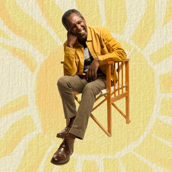 Lemn Sissay sits on a wooden chair, smiling and resting his head on his hand, wearing a yellow jacket in front of a paper-textured illustration of a yellow sun.