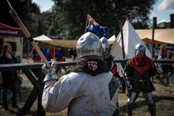 a group of people in armour holding weapons and fighting each other in a field