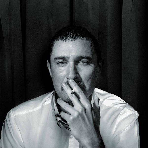 Black and white image of Tom Rosenthal smoking in the style of the Arctic Monkeys' album cover for Whatever People Say I Am, That's What I'm Not.