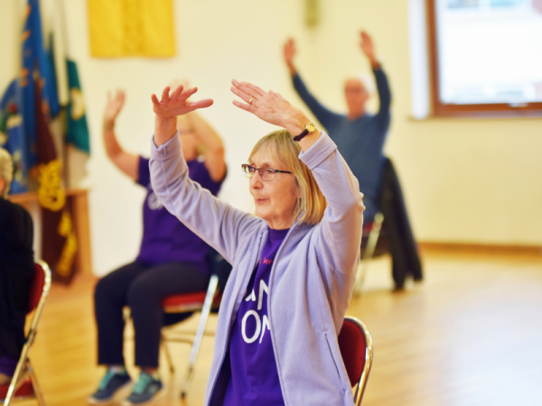 A lady is dancing in a chair with her arms above her head