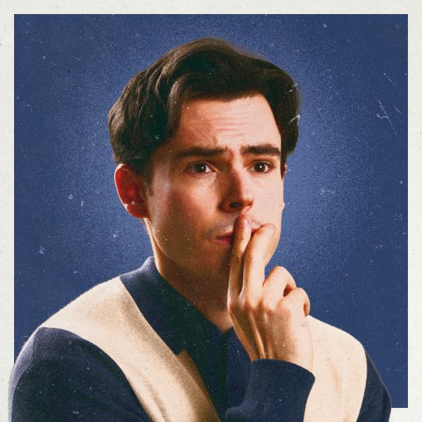 Rhys James looks pensive and holds two fingers to his lips, photographed against a blue backdrop with grain applied over the top.