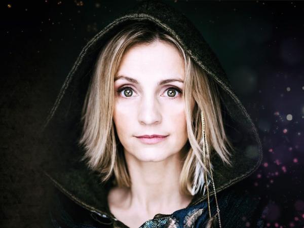 A women with medium length light coloured hair, wearing a black hooded robe.