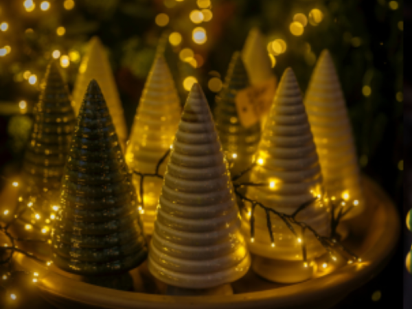 A tray of ceramic Christmas trees with fairy lights in the background.