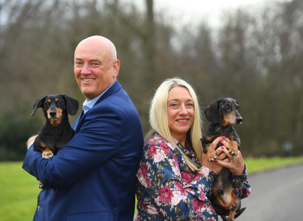 Alan Lazenby holding sausage dog and Dee Lazenby holding their other sausage dog.