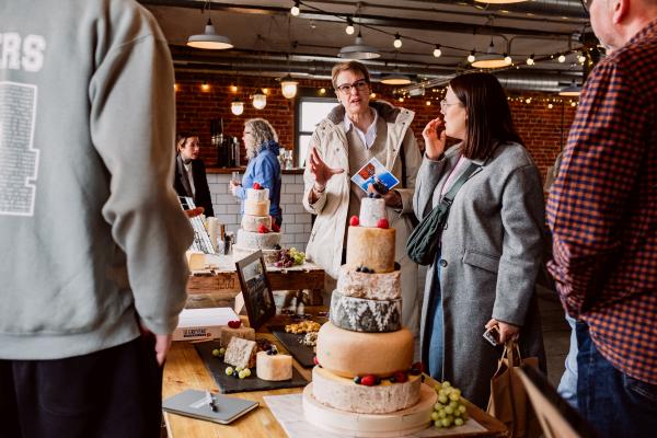 People stand talking next to a tall tower of cheese wheels