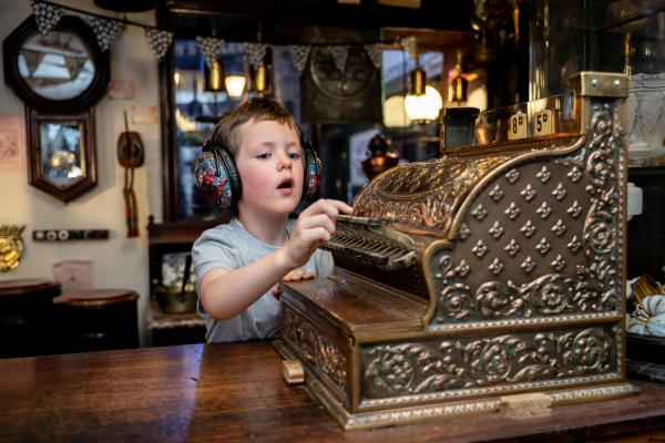 Child wearing ear defenders plays with an ornate old fashioned shop till