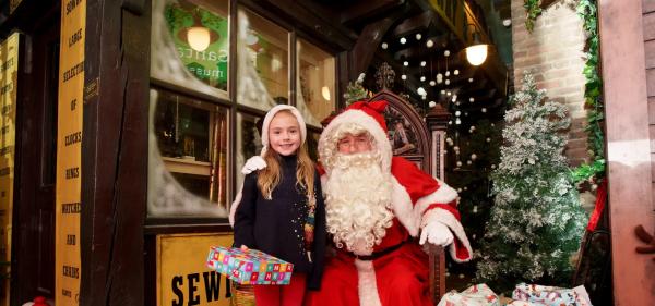 A colour photograph of a child in a seasonal outfit posing with Santa in the Victorian Streets at Abbey House Museum