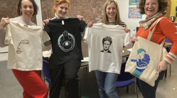 A group of smiling women show off their screen printed tees and totes