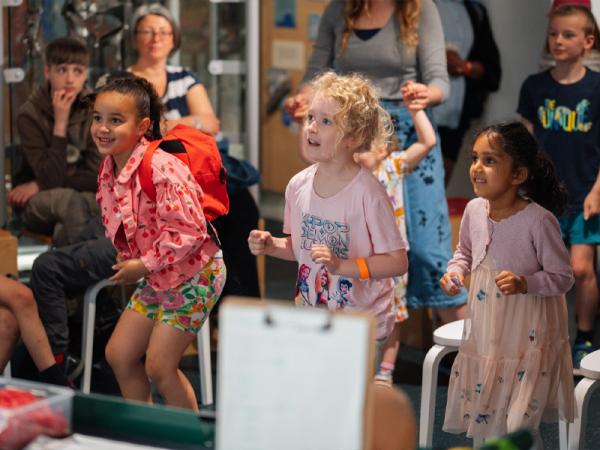 Three young children taking part in an activity in a museum all smiling at something off screen.