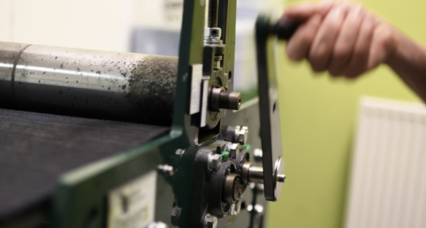 The handle of an etching press being turned