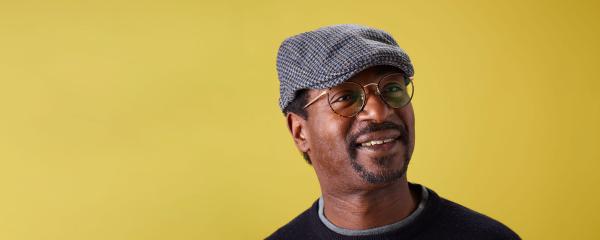 An image of Chris Dawkins wearing a flat cap and glasses, smiling.