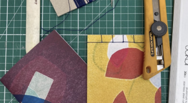 Handmade books with colourful abstract covers alongside craft knives and tools for bookbinding