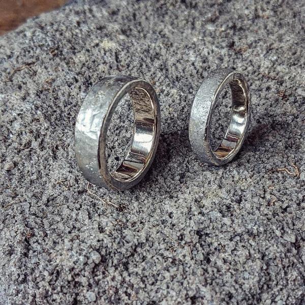 Two silver rings stand on their outer edge, on a grey fluffy surface. they are chunky with texture on the outside and a smooth inside.