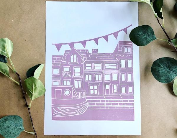 A purple lino print of a canal boat in front of a row of town houses, with bunting hanging over the top.