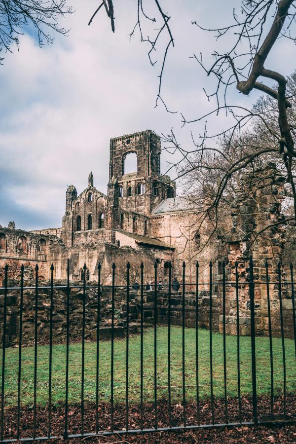 View of Kirkstall Abbey from behind a wrought iron gate.